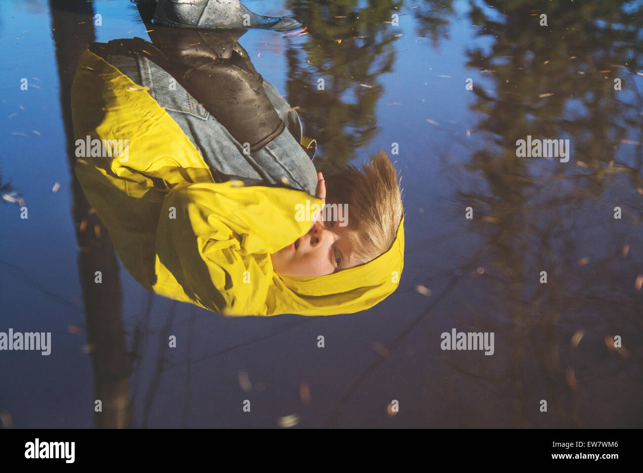 La riflessione del ragazzo in cappotto di pioggia cercando in una pozza di acqua Foto Stock