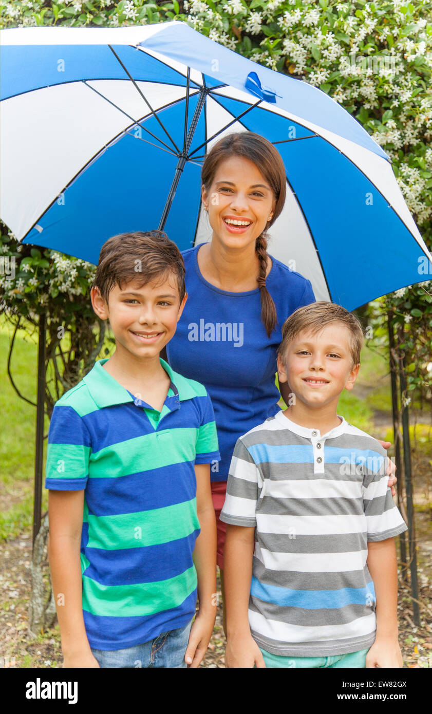 Unico madre ispanica con due ragazzi giocare sotto la pioggia Foto Stock