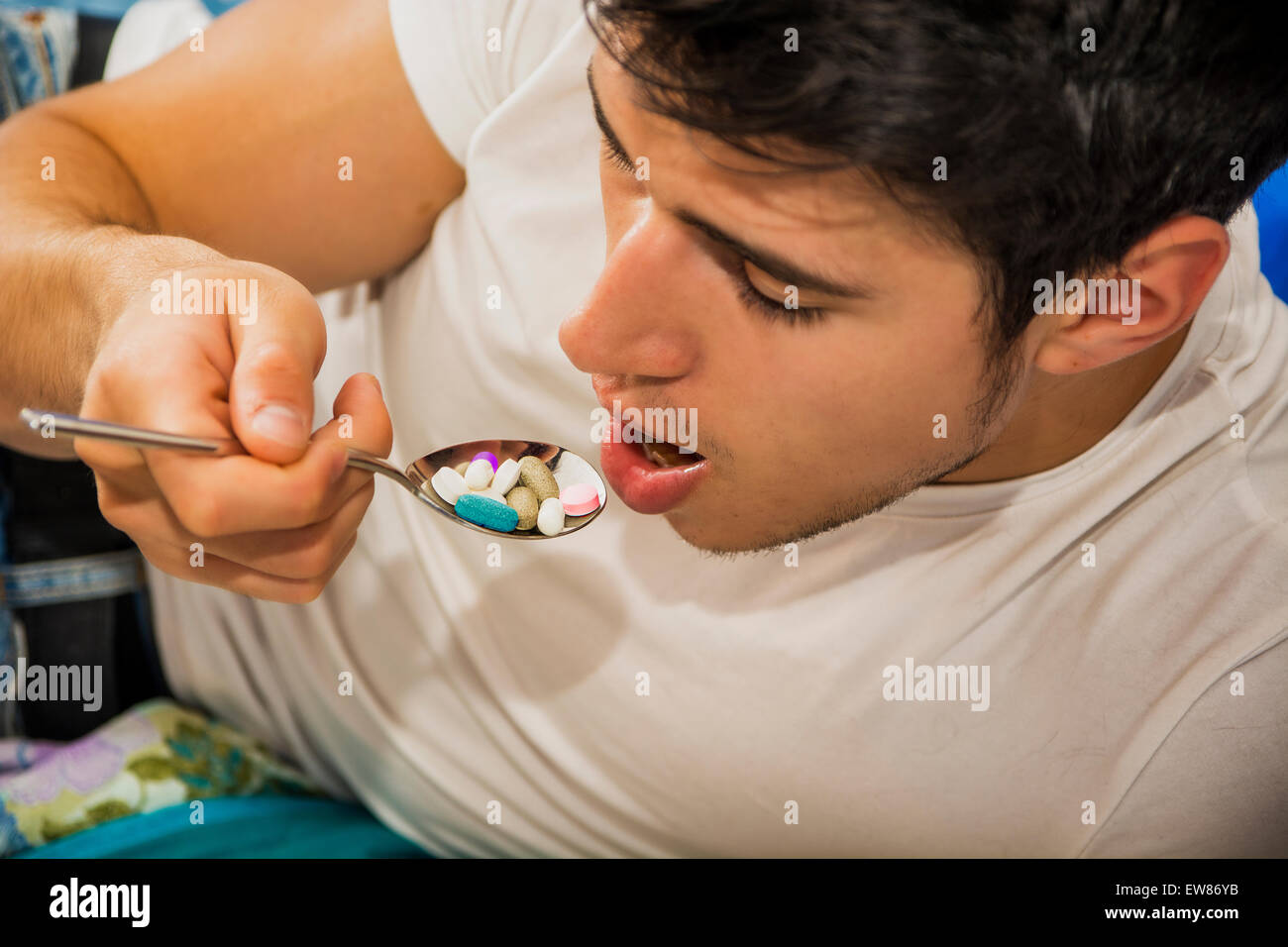 Attraente giovane uomo nel letto di mangiare un cucchiaio colmo di medicina, compresse e pillole Foto Stock
