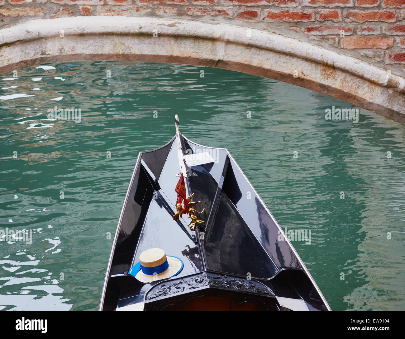 Gondola passando sotto un ponte con la bandiera veneziana e il cappello di paglia del gondoliere Venezia Veneto Italia Europa Foto Stock