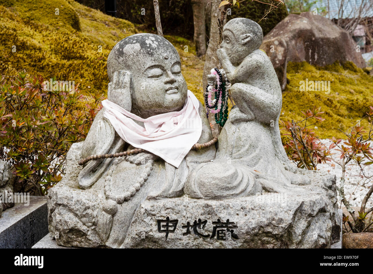 Giappone, Miyajima. Tempio Daisho-in. Piccola statua di Jizo di un monaco buddista reclinato con bib rosso e una scimmia sussurrante seduto accanto a lui mangiare. Foto Stock
