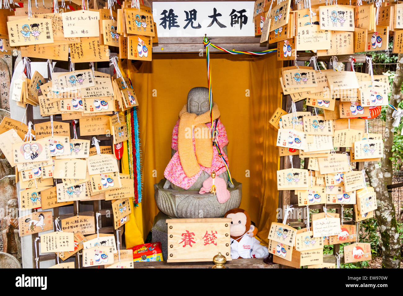 Giappone, Miyajima, tempio Daisho-in. Statua Bibbed Jizo su piedistallo in piccolo recinto di santuario con masse di assi ema appesi su entrambi i lati. Foto Stock