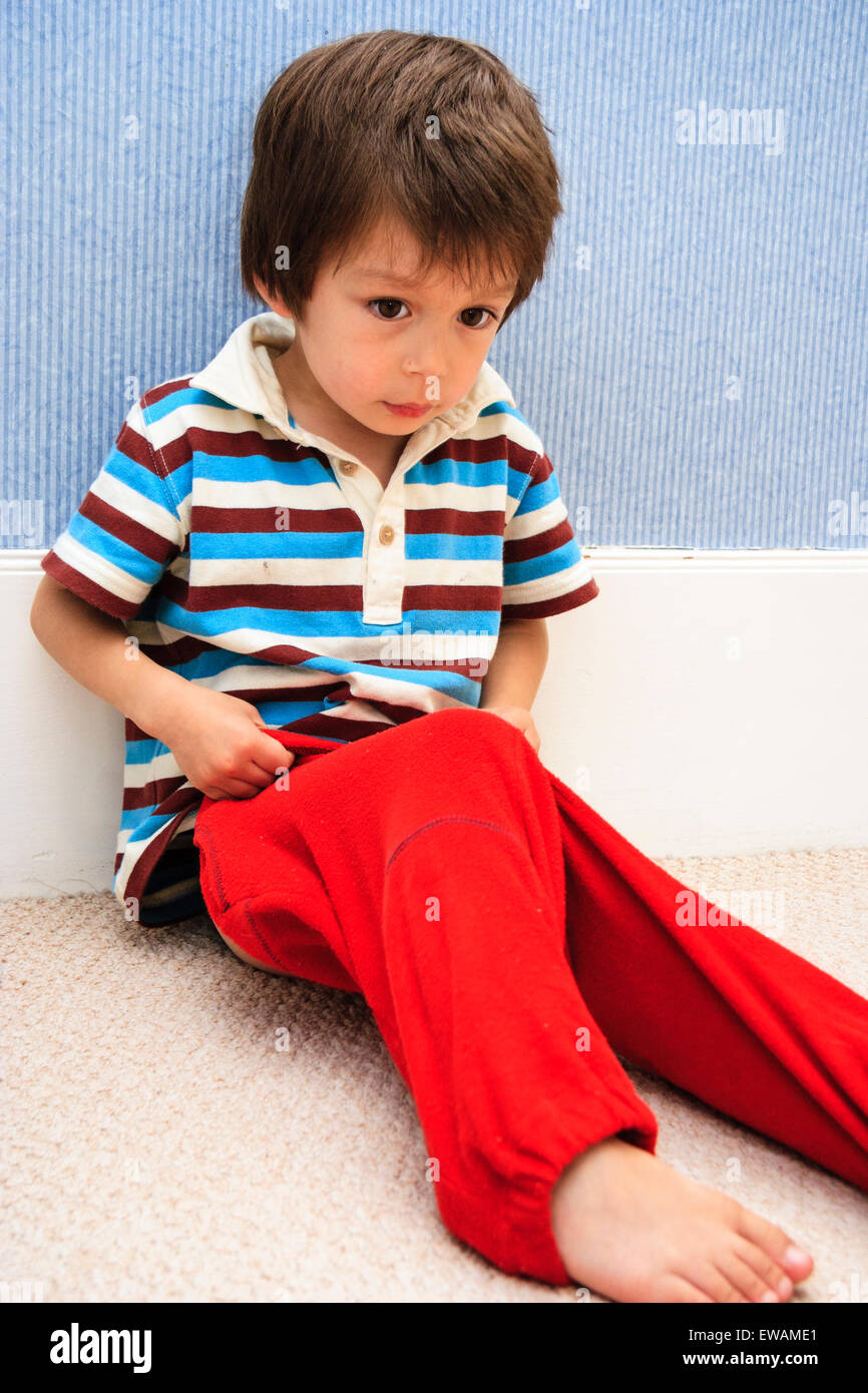 Bambino caucasico, boy, 3-4 anni. In ambienti chiusi, seduti su un tappeto  contro il battiscopa e parete, tirando su un paio di pantaloni rossi Foto  stock - Alamy