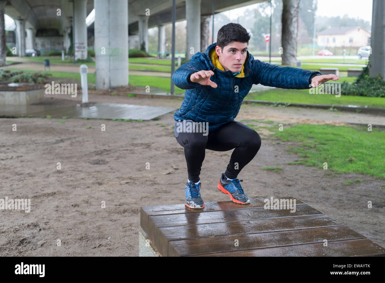 L'uomo squatting in un parco in un giorno di pioggia Foto Stock