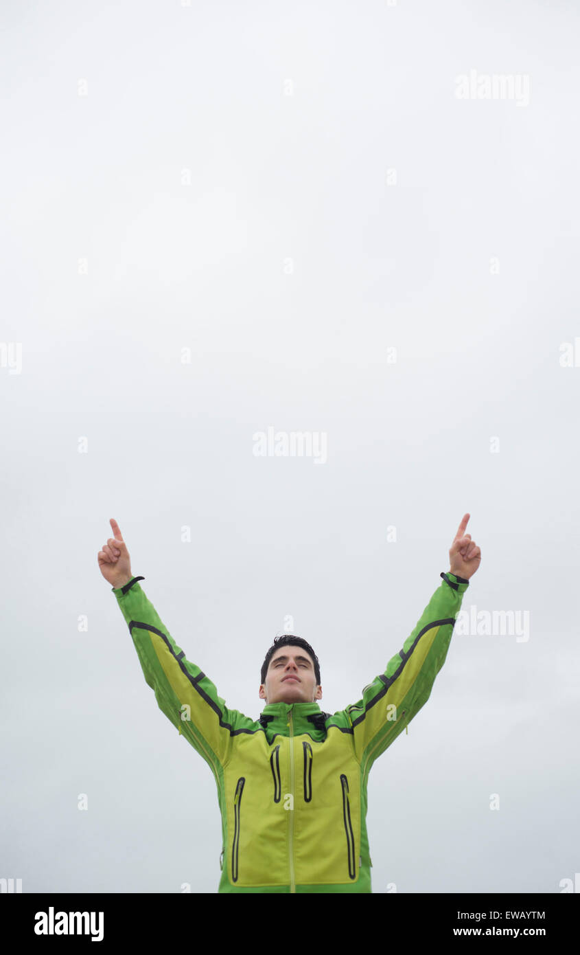 Runner uomo con le braccia alzate in segno di vittoria simbolo contro il cielo nuvoloso Foto Stock