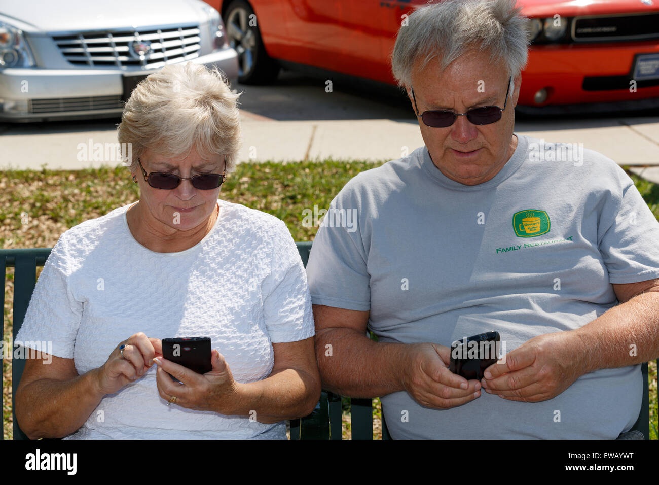Coppia senior seduti fianco a fianco texting sui loro telefoni cellulari Foto Stock