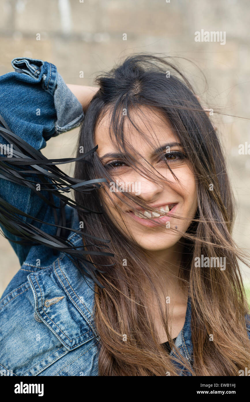 Ritratto di una giovane donna bruna all'esterno. La donna è sempre sorridente e ha capelli tousled Foto Stock