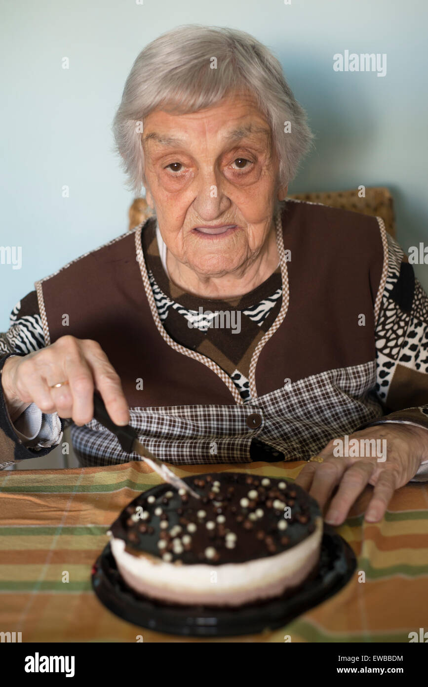 Donna anziana il taglio la sua torta di compleanno a casa Foto Stock