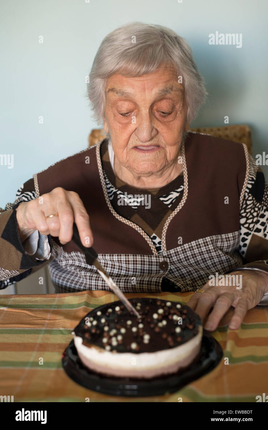 Donna anziana il taglio la sua torta di compleanno a casa Foto Stock