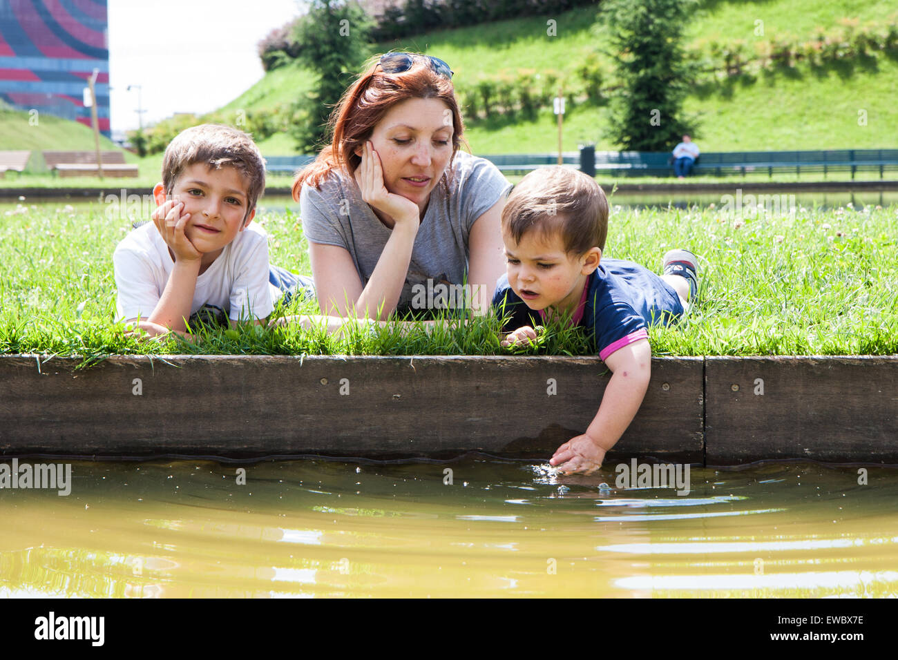 Ritratto di madre con due bambini sdraiati sull'erba sulla sponda di un laghetto Foto Stock
