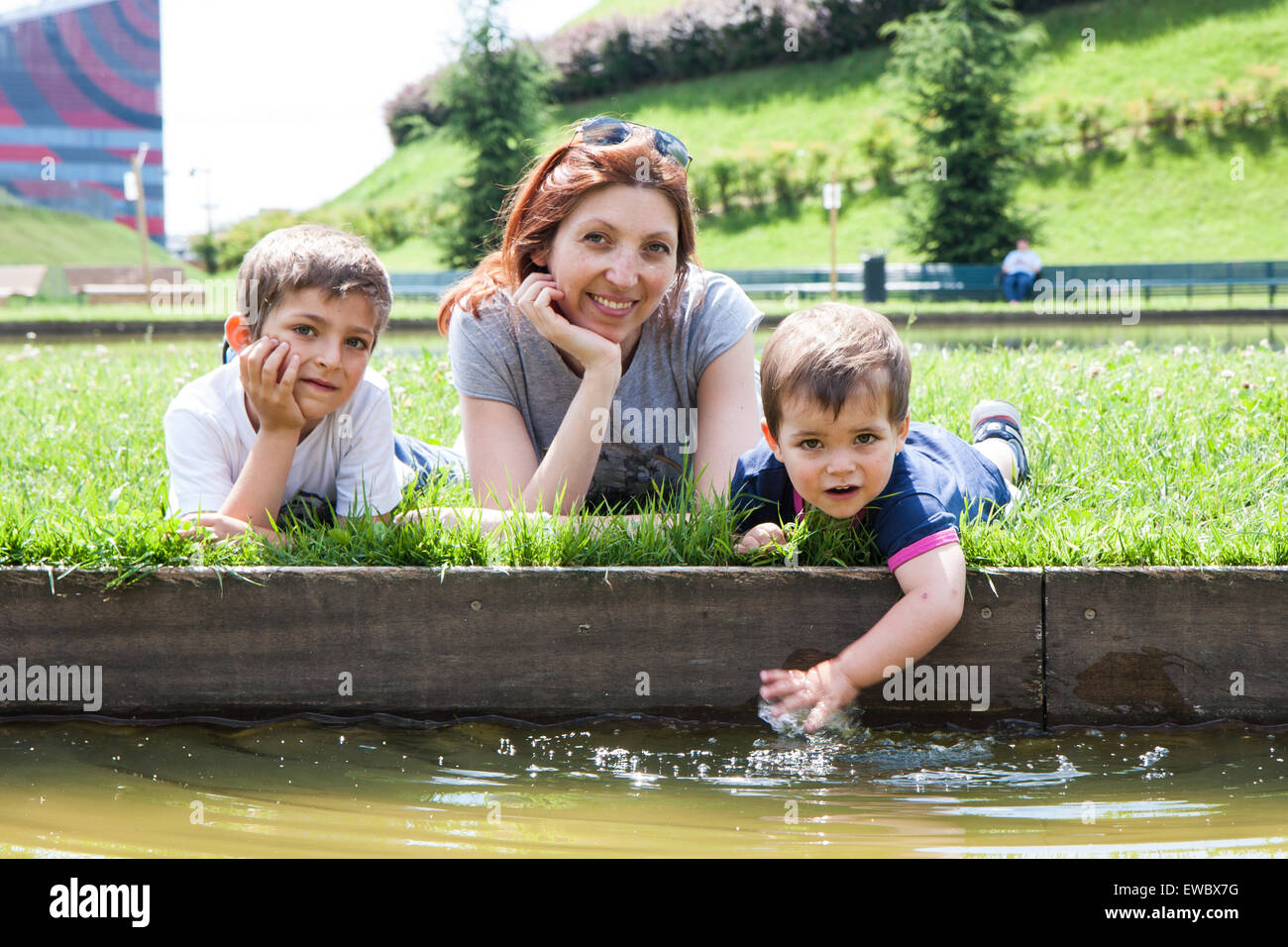 Ritratto di madre con due bambini sdraiati sull'erba sulla sponda di un laghetto Foto Stock