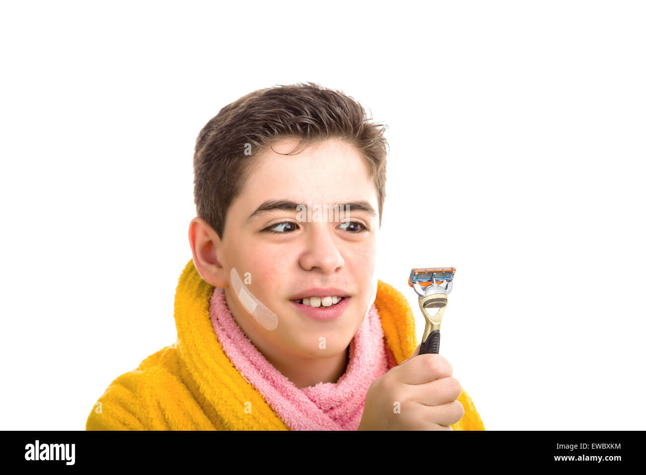 Liscia caucasico-pelato ragazzo indossa un accappatoio giallo con un asciugamano rosa intorno al suo collo: ha alcune patch sul suo volto sorridente e la guarda con gli occhi incrociati presso il rasoio ha utilizzato per la rasatura Foto Stock