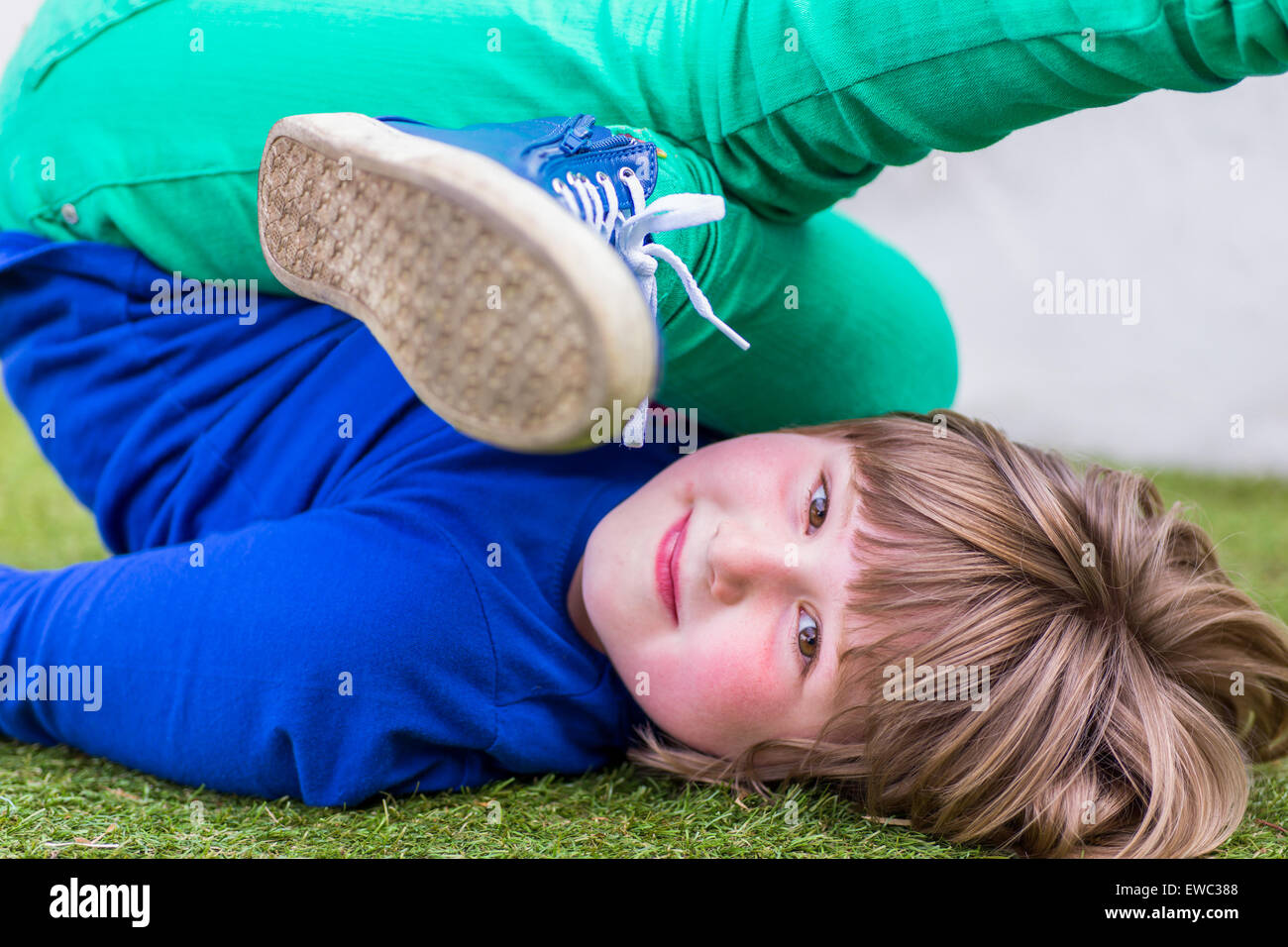 Piegate la ragazza europea sdraiata su erba al parco giochi Foto Stock