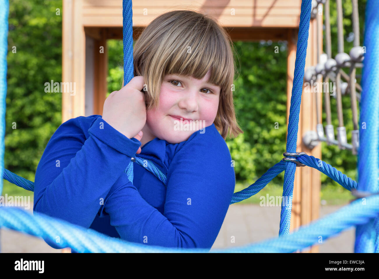 Giovane ragazza caucasica giocando in web di corde blu al parco giochi Foto Stock