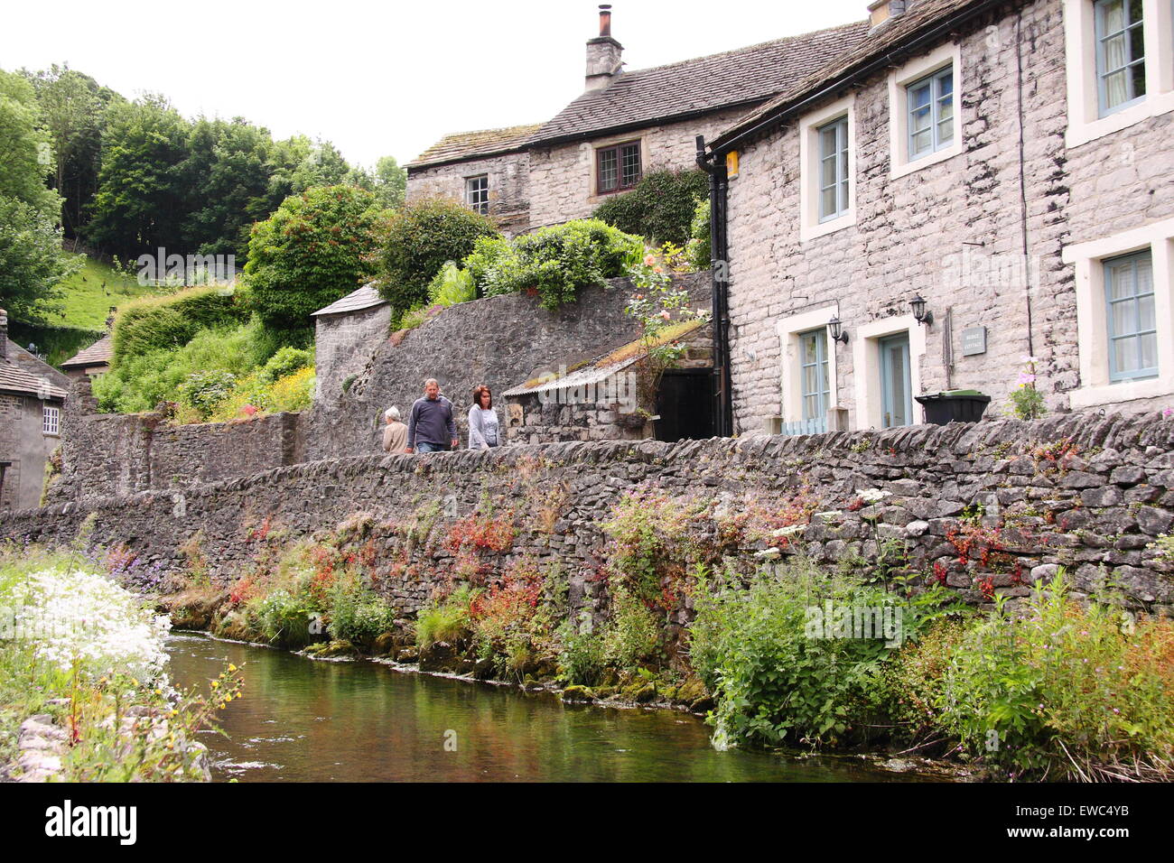 Walkers passano da una pietra a secco sulla parete Peakshole acqua nel cuore di Castleton villaggio nel distretto di Peak Derbyshire Regno Unito estate Foto Stock