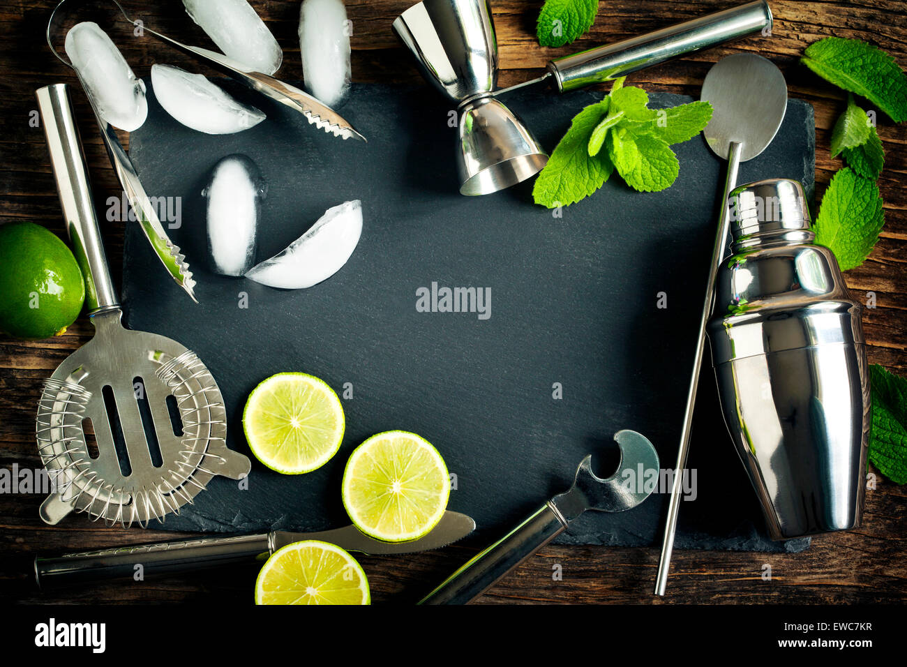 Set di accessori bar e gli ingredienti per la realizzazione di un cocktail disposti su un sfondo di legno nero con bordo per spazio di copia Foto Stock