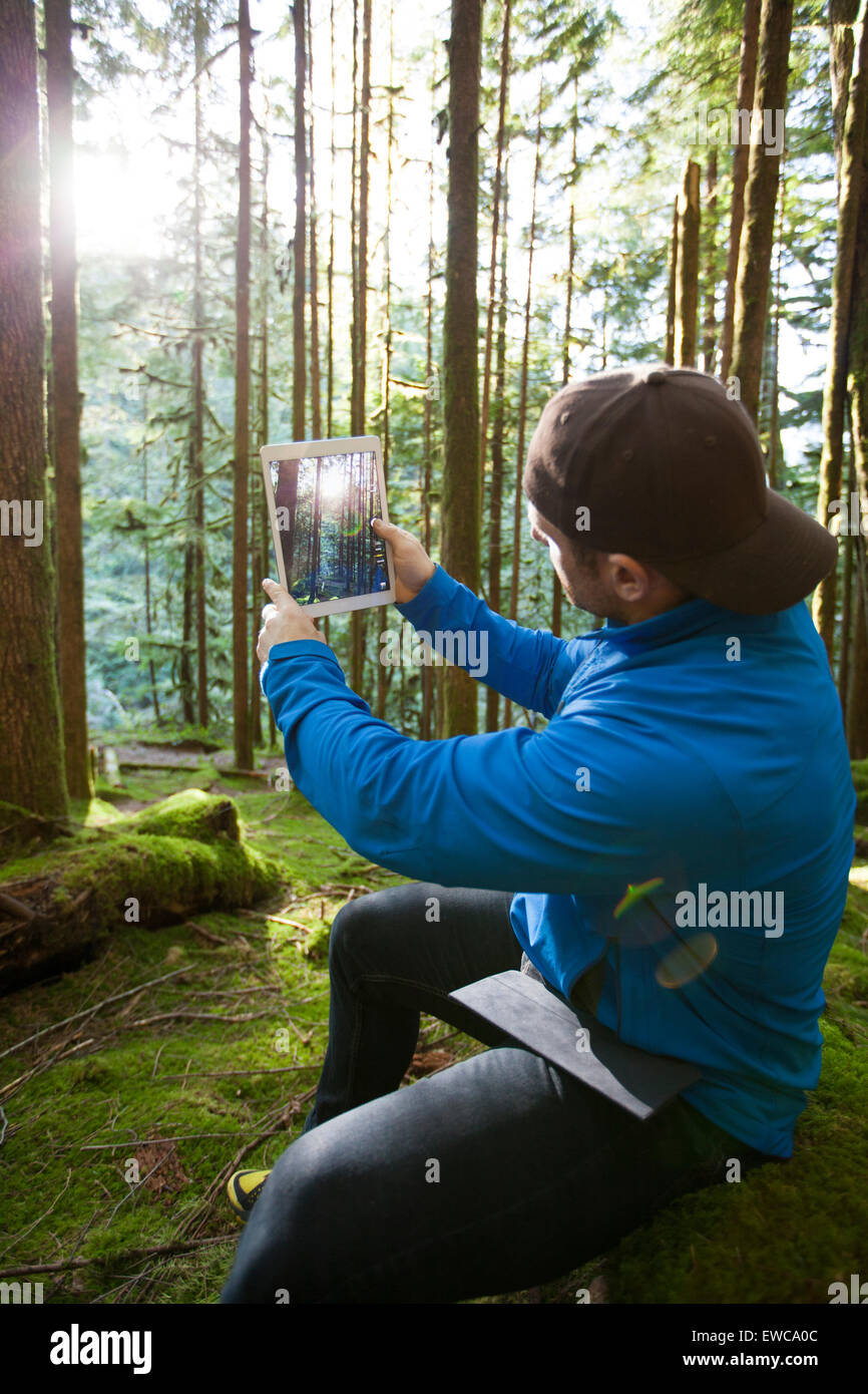 Un uomo utilizza un tablet per scattare una foto del sole del mattino che splende attraverso la foresta. Foto Stock