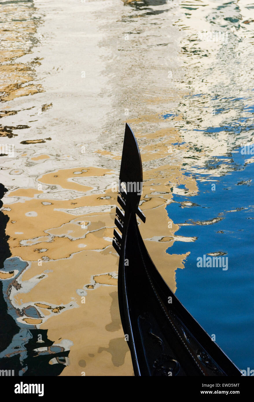 L'arco di una gondola veneziana taglia i riflessi nel canale Foto Stock