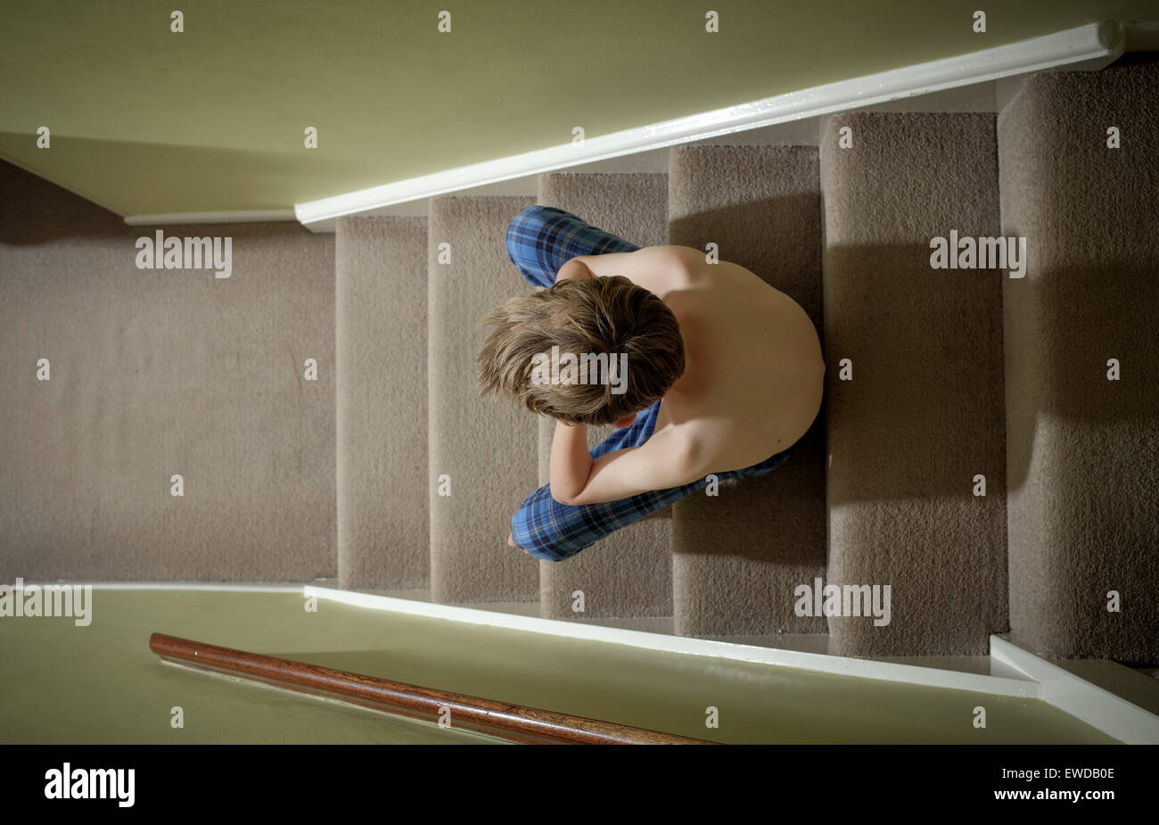 Un bambino seduto sulle scale con la testa tra le mani cercando sconvolto Foto Stock