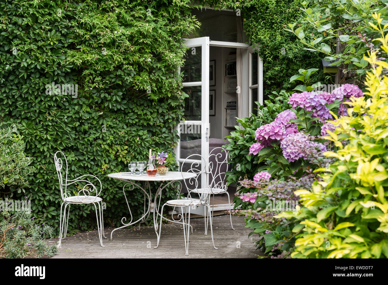 Finestre francesi che conducono al giardino bianco con mobili in ferro battuto con rododendri e jasmin muri rivestiti Foto Stock