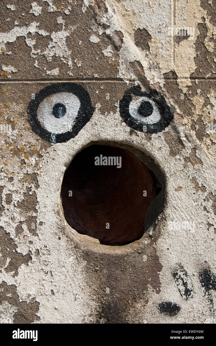 Arte di strada - graffiti attorno ad un foro in una parete per contribuire a creare una faccia con una grande bocca Foto Stock