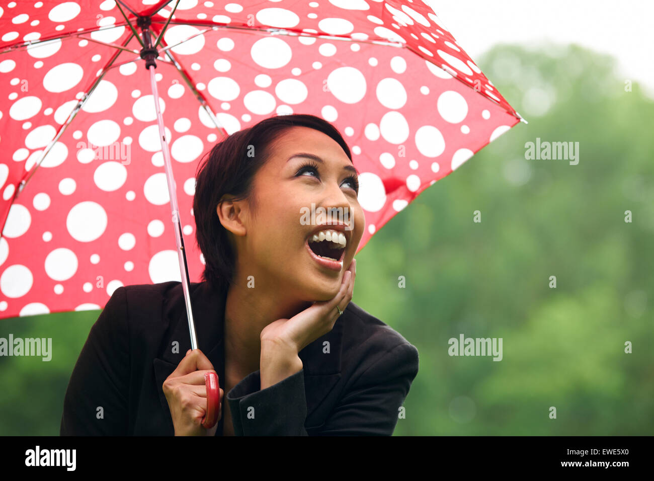 Giovane donna si ripara dalla pioggia sotto ombrellone Foto Stock