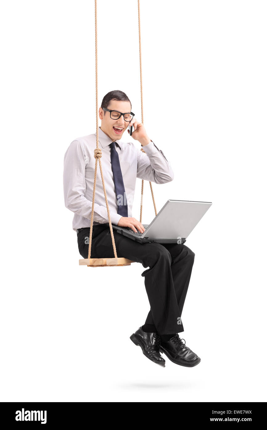 Colpo verticale di un giovane uomo che lavora su un notebook seduto su una tavola di legno di oscillazione e di parlare sul suo telefono cellulare Foto Stock