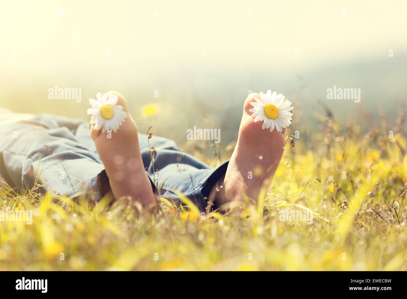 Bambino con la margherita tra le dita dei piedi giacente in prato rilassante in un sole estivo Foto Stock