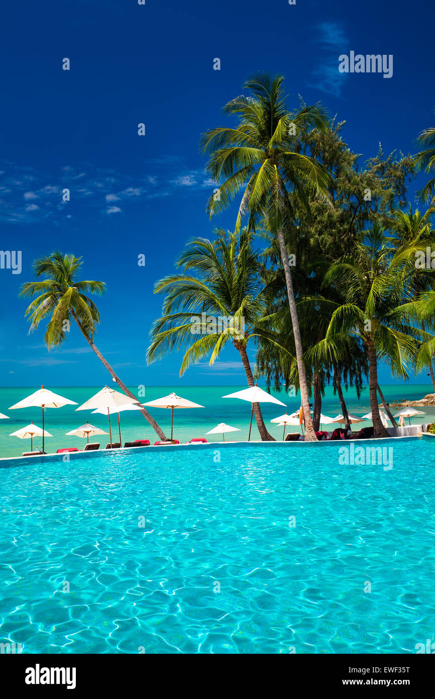 Grande piscina a sfioro sulla spiaggia con palme e ombrelloni Foto Stock