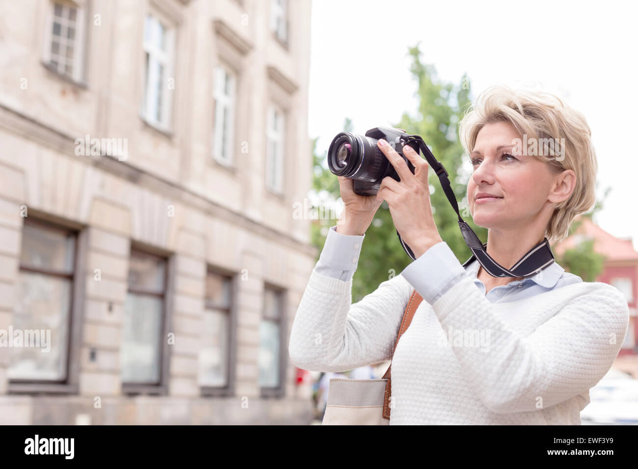 Donna di mezza età fotografando attraverso la fotocamera digitale in città Foto Stock