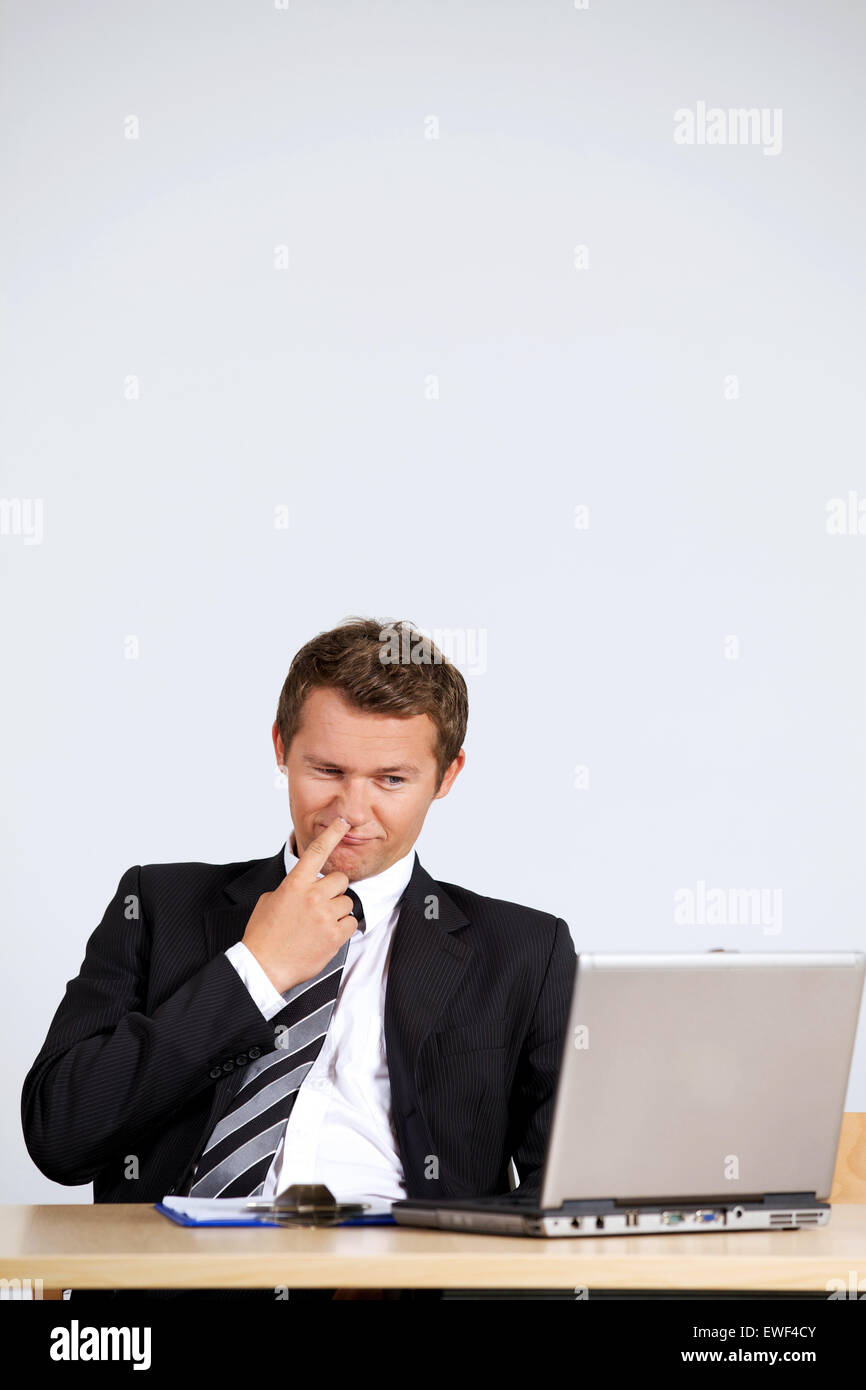 Imprenditore picking naso, guardando il computer portatile in ufficio Foto Stock