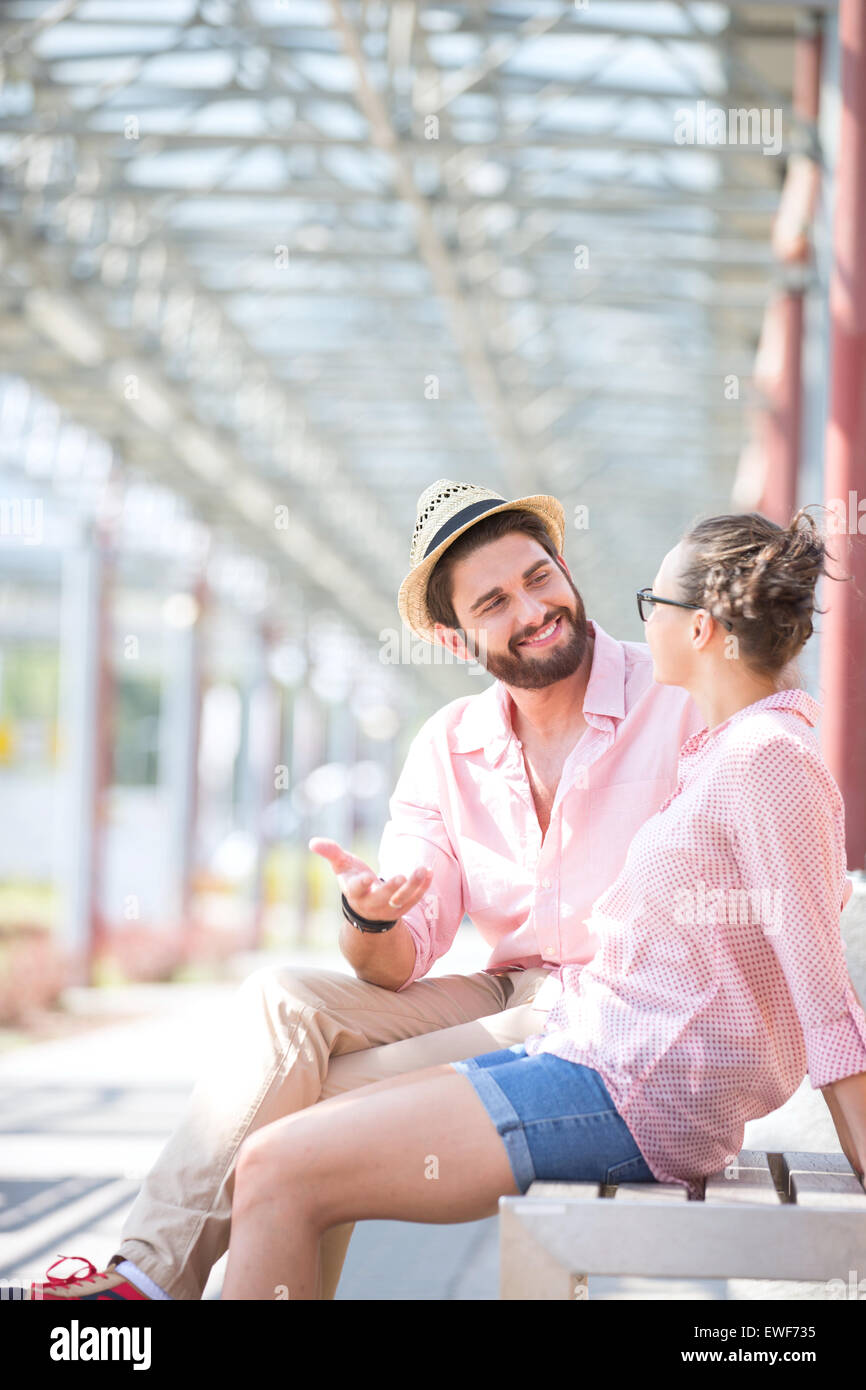 Felice l'uomo a parlare con una donna durante la seduta sul banco sotto ombra Foto Stock