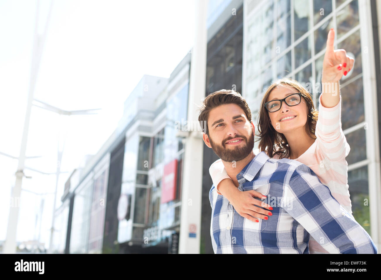 Donna sorridente rivolto lontano mentre godendo piggyback ride su uomo in città Foto Stock