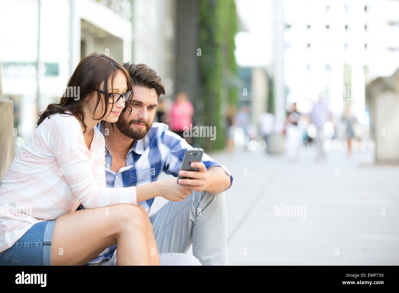 Paio utilizzando smart phone insieme mentre è seduto sui gradini in città Foto Stock
