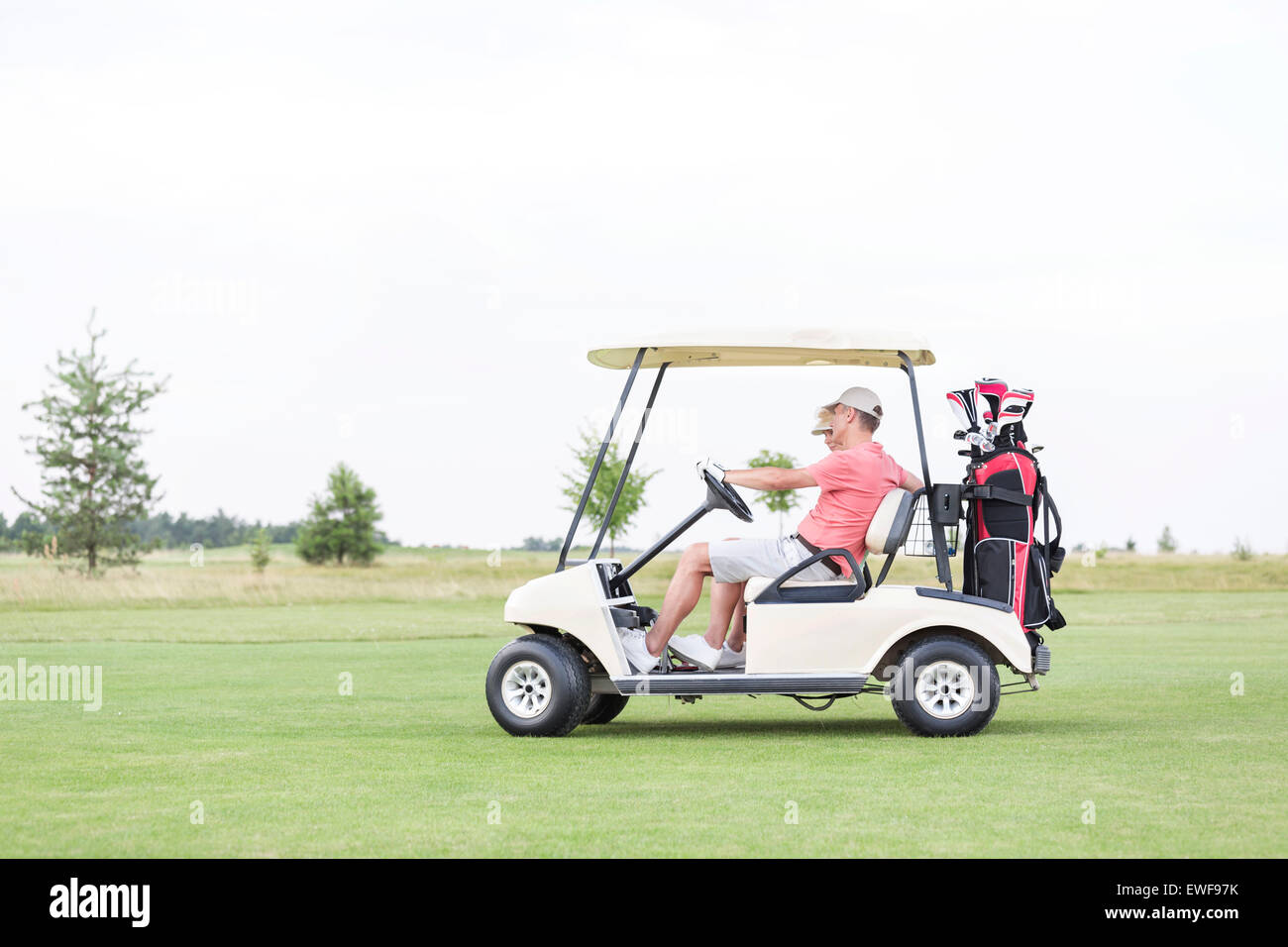 Vista laterale del giovane seduto in golf cart contro il cielo chiaro Foto Stock