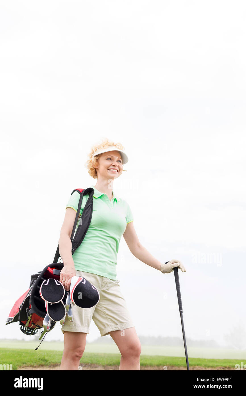 Basso angolo di vista sorridente golfista femmina in piedi contro il cielo chiaro Foto Stock