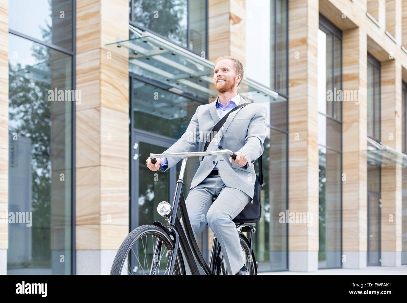 Imprenditore sorridente bicicletta equitazione all'esterno dell'edificio Foto Stock