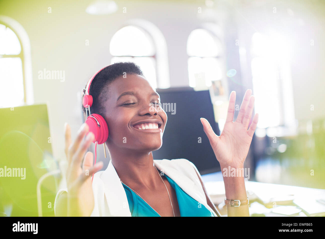 Sorridente imprenditrice ascoltando musica sulle cuffie in ufficio con gli occhi chiusi Foto Stock