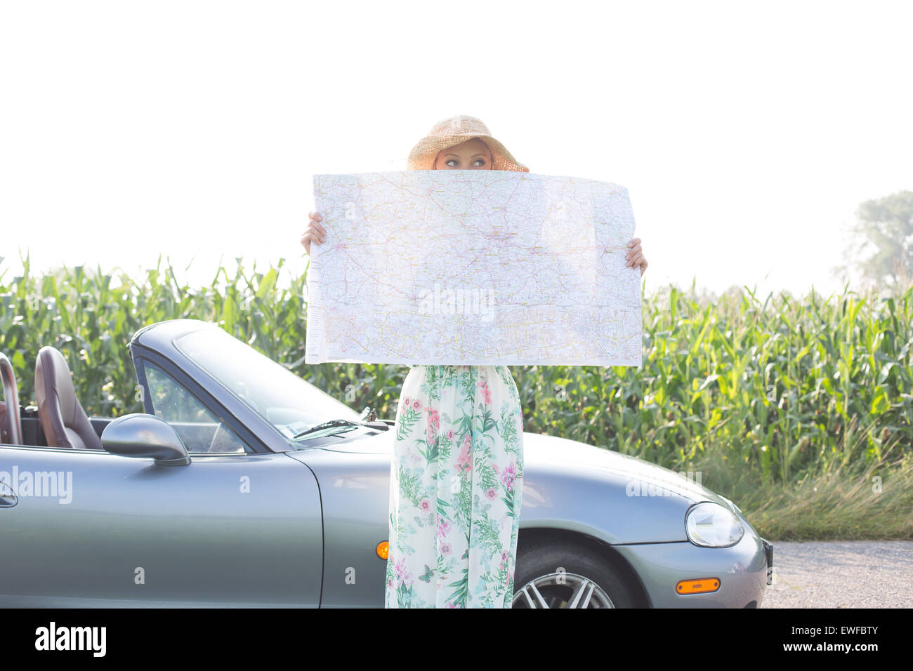 La donna nasconde il viso con mappa da convertible contro il cielo chiaro Foto Stock