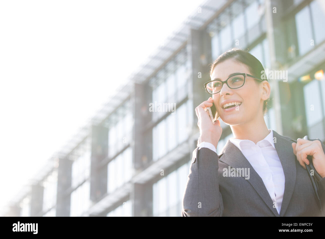Basso angolo vista di felice imprenditrice tramite telefono cellulare al di fuori di edificio per uffici Foto Stock