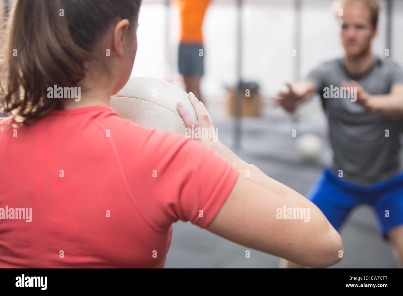 Vista posteriore della donna medicina lanciando la palla verso l'uomo in palestra crossfit Foto Stock