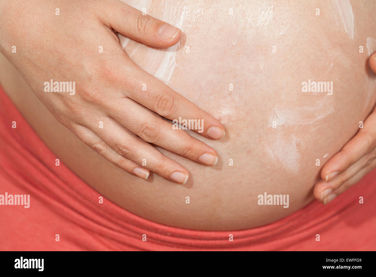 Donna incinta mettendo la lozione sulla pancia Foto Stock