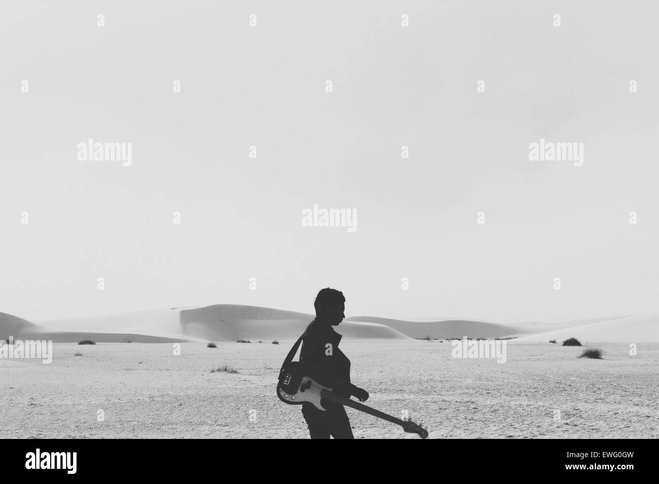 Un musicista che trasporta una chitarra basso attraverso un paesaggio desertico, illustrando il contrasto tra l'ambiente arido e lo strumento musicale, possibilmente per una performance o una registrazione. Foto Stock
