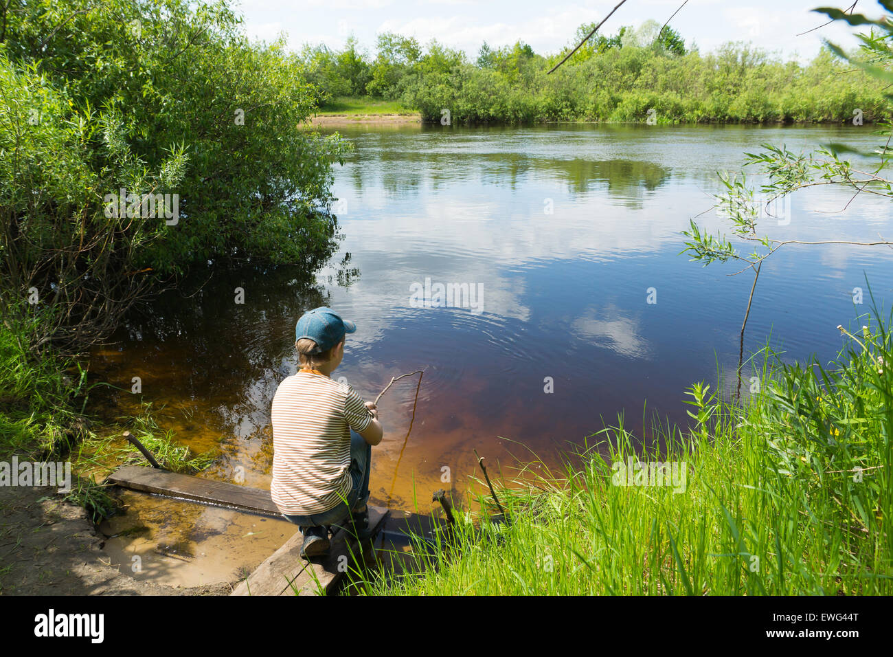 Il ragazzo in un tappo le catture di pesci nel fiume su un self made asta Foto Stock