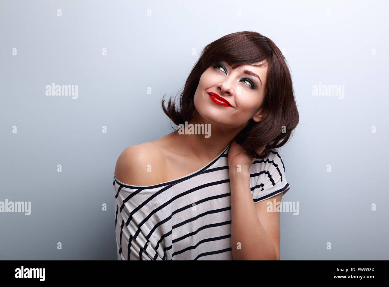 Felice di capelli corti trucco donna pensando e guardando in alto su sfondo blu Foto Stock