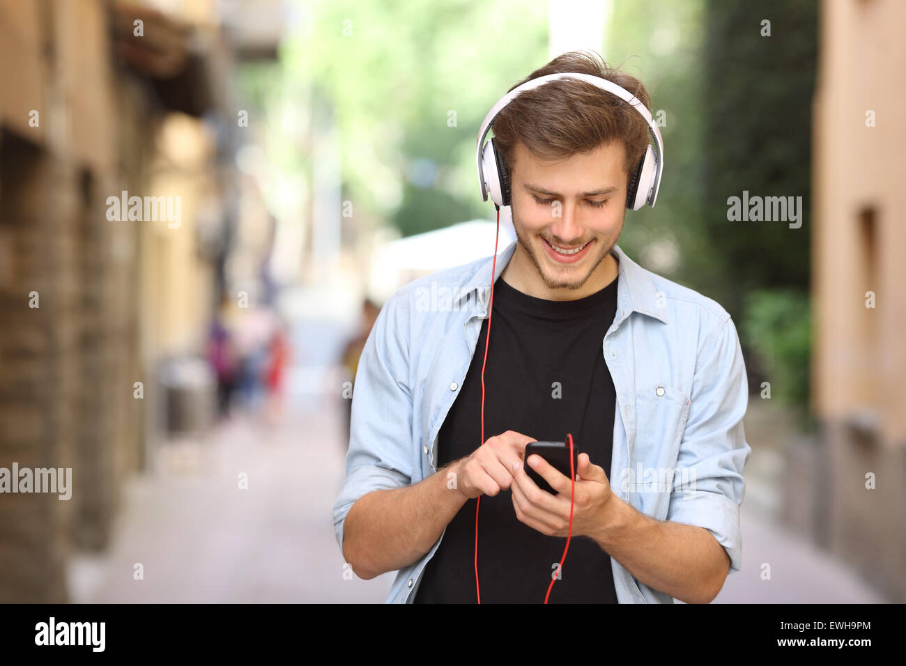 Happy guy camminare e utilizzando un telefono intelligente per ascoltare musica con le cuffie Foto Stock