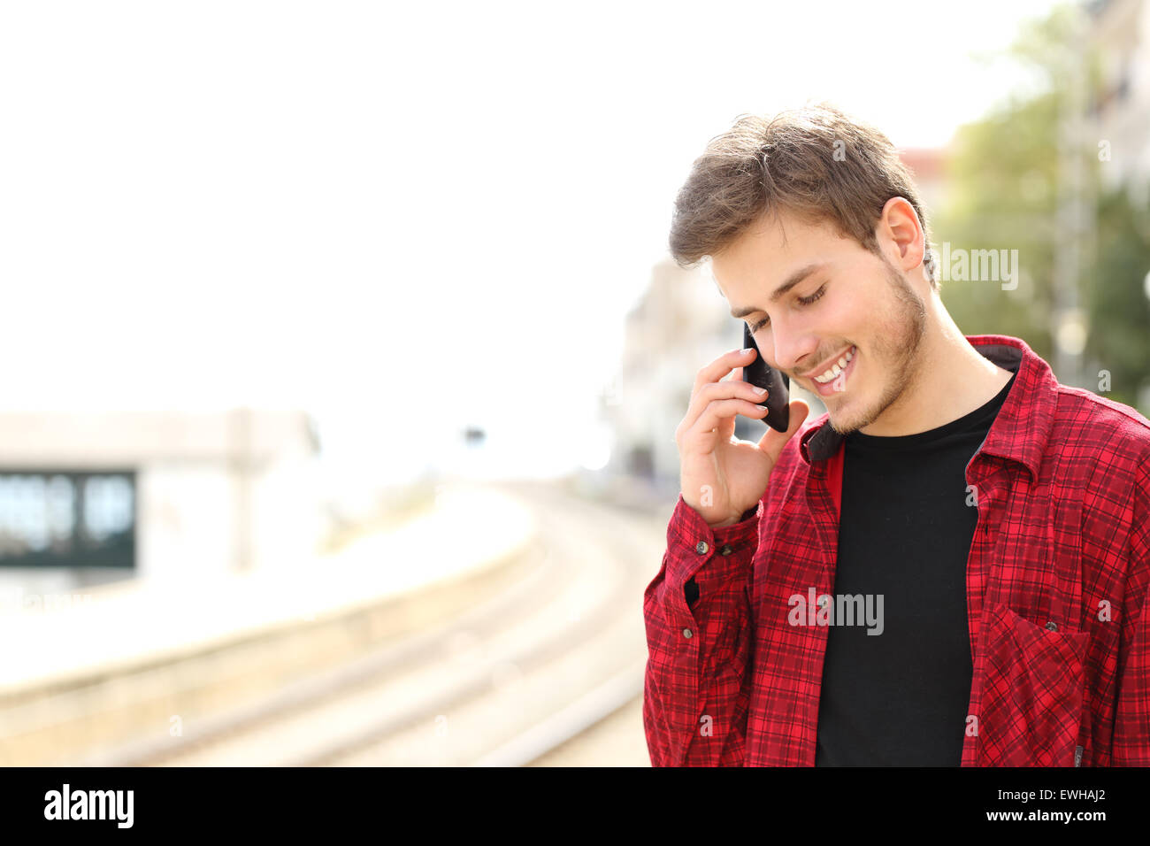 Traveler teen guy chiamando al telefono cellulare in una stazione ferroviaria mentre egli è in attesa Foto Stock