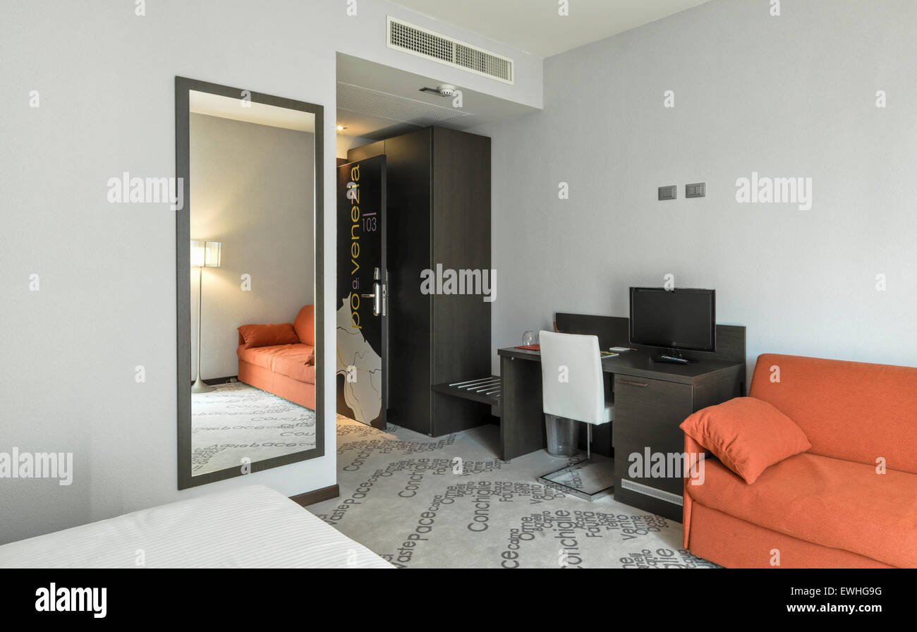 Interno di entrata della moderna camera da letto in hotel con divano arancio e scrivania Foto Stock