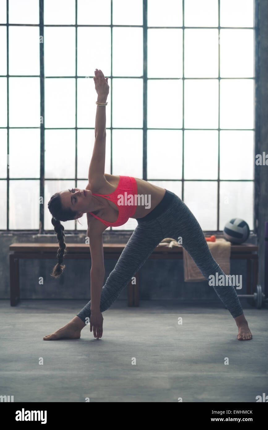 Un forte e muscoloso donna sta facendo il triangolo esteso pongono nello yoga in una città loft palestra. Foto Stock
