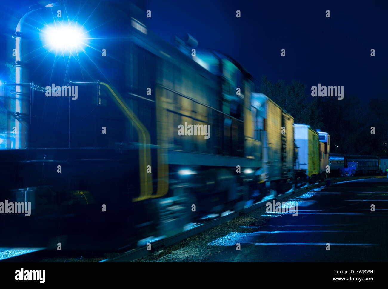 Una vecchia locomotiva diesel e nolo auto glow in una misteriosa blu sotto le luci della notte di un railyard Foto Stock